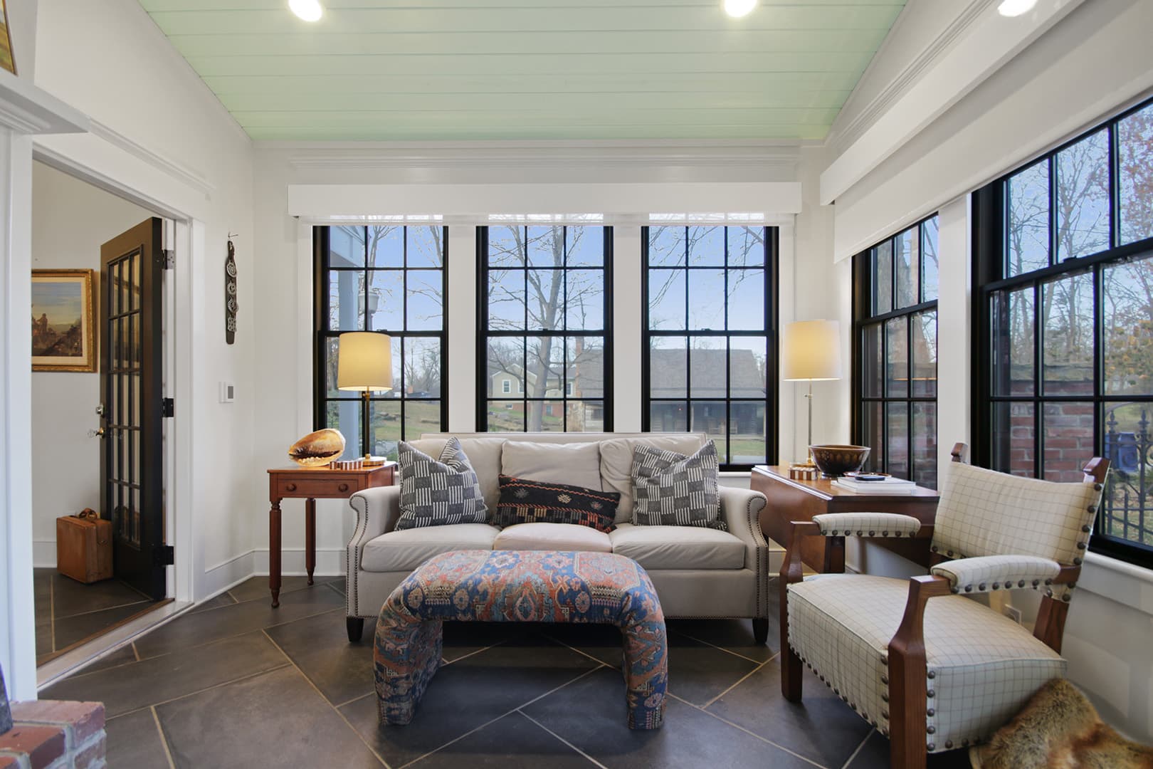 A serene sunroom with a vaulted ceiling,, a cozy sofa, an armchair, and large windows offering a peaceful view of the outdoors.