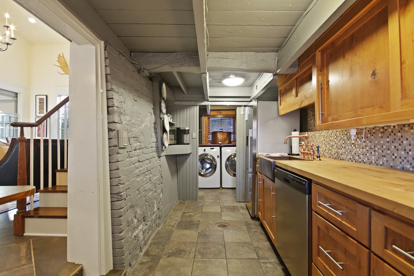 A galley-style kitchen a long countertop, wooden cabinets, and a washing machine and clothes dryer visible at the end.