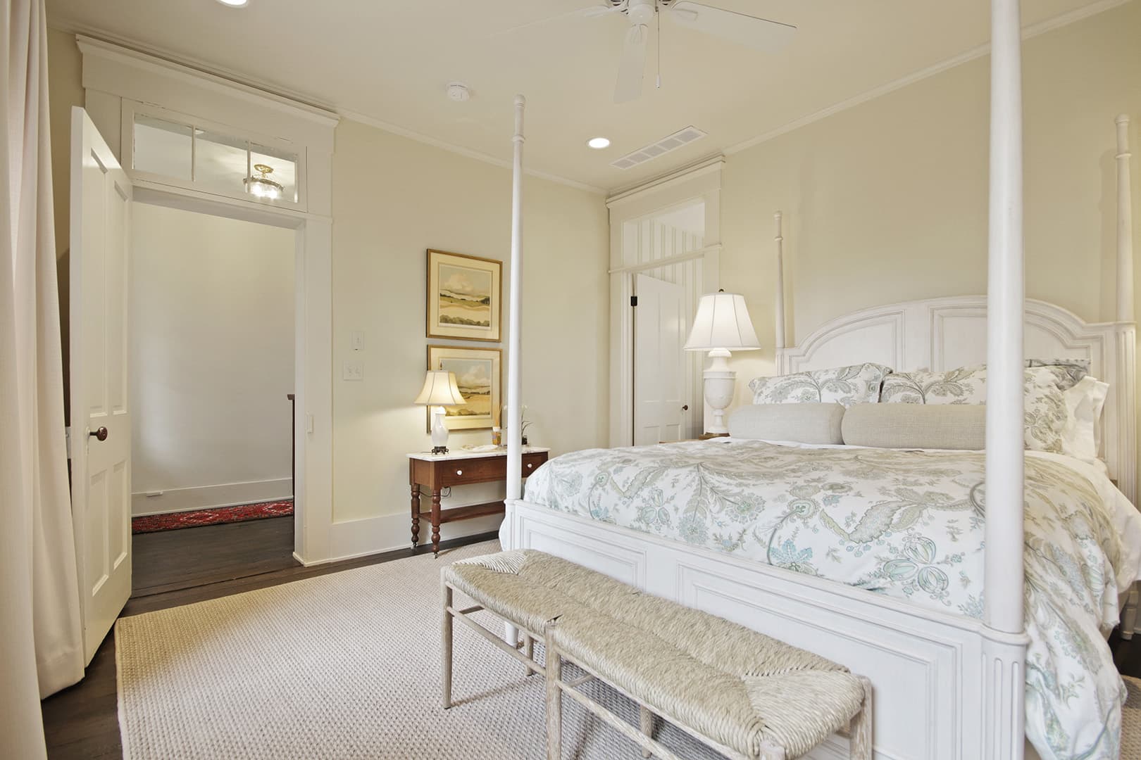 A classic bedroom featuring a white four-poster bed with floral bedding, two bedside tables with lamps, and a light-colored rug.