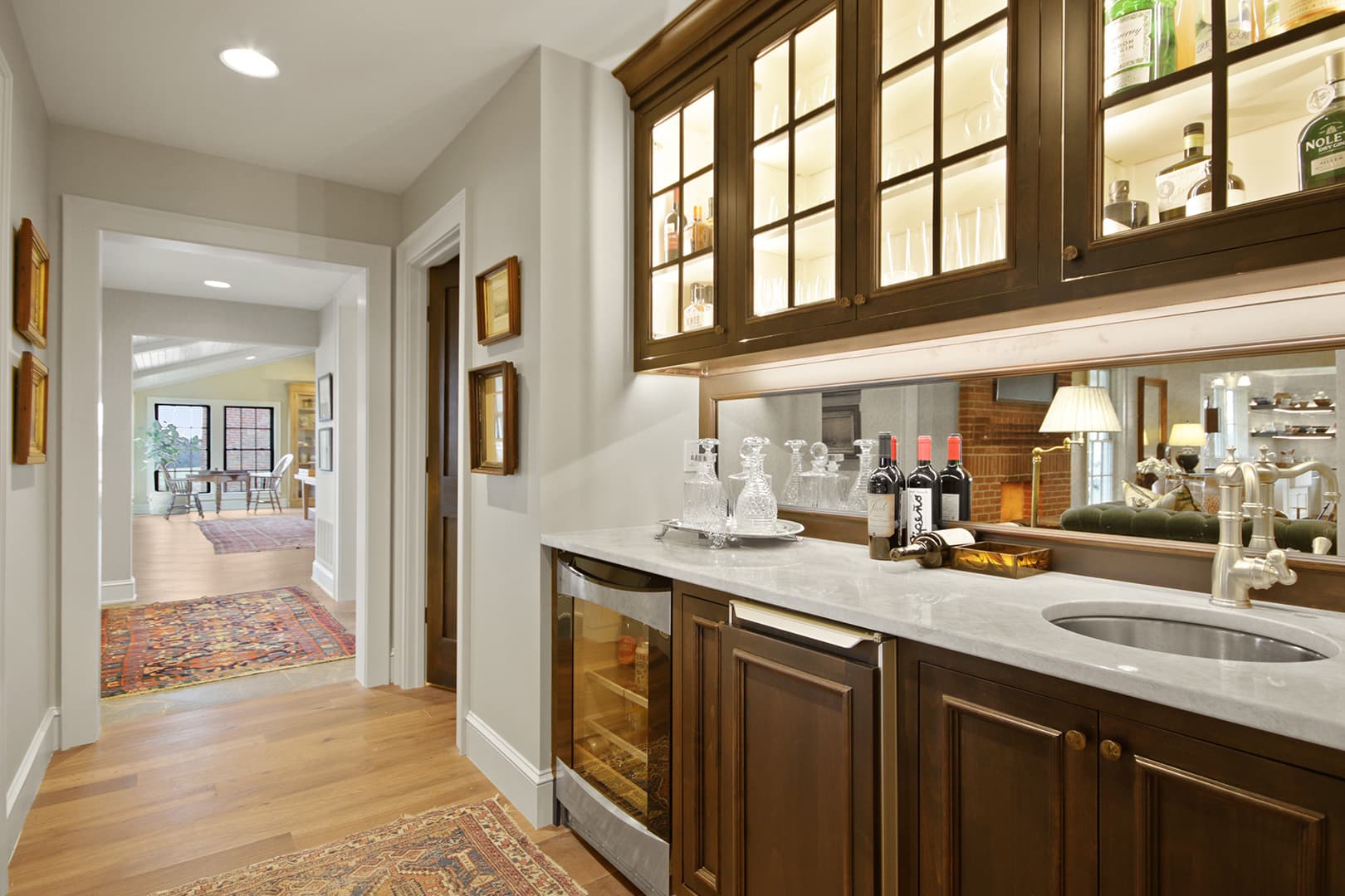 Elegant kitchen with dark wood cabinetry, glass-fronted illuminated upper cabinets, and a spacious counter with sink and beverage fridge.