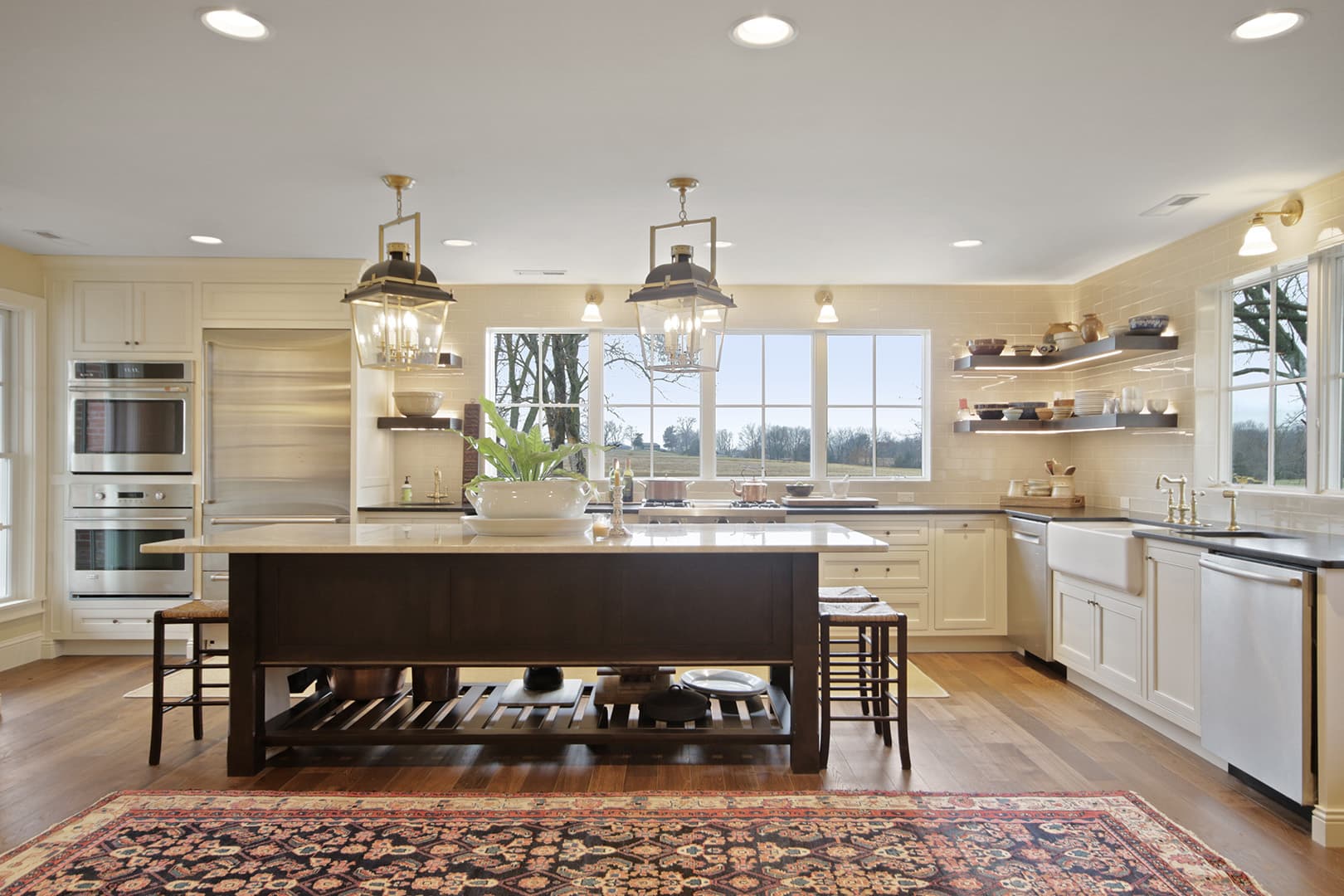 A spacious, bright open-concept kitchen with a large island, traditional cabinetry, modern lighting, and a decorative rug on hardwood floors.