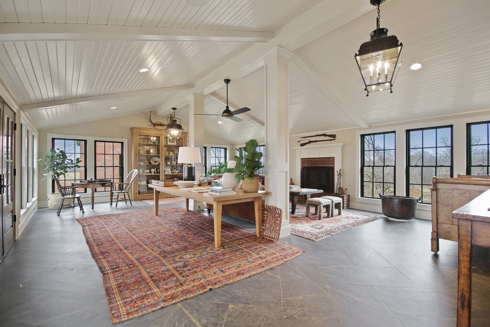 A spacious open-concept living area with a vaulted white ceiling, exposed beams, ample natural light, and eclectic furniture.